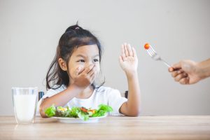 child who does not like to eat vegetables is pushing a fork away
